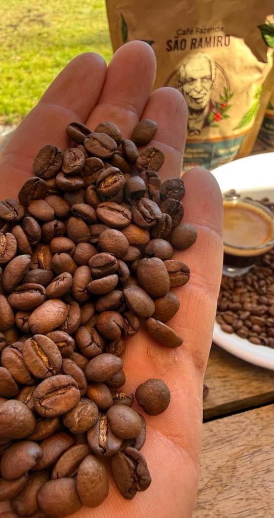Mão segurando grãos de café torrado, com o pacote ao fundo