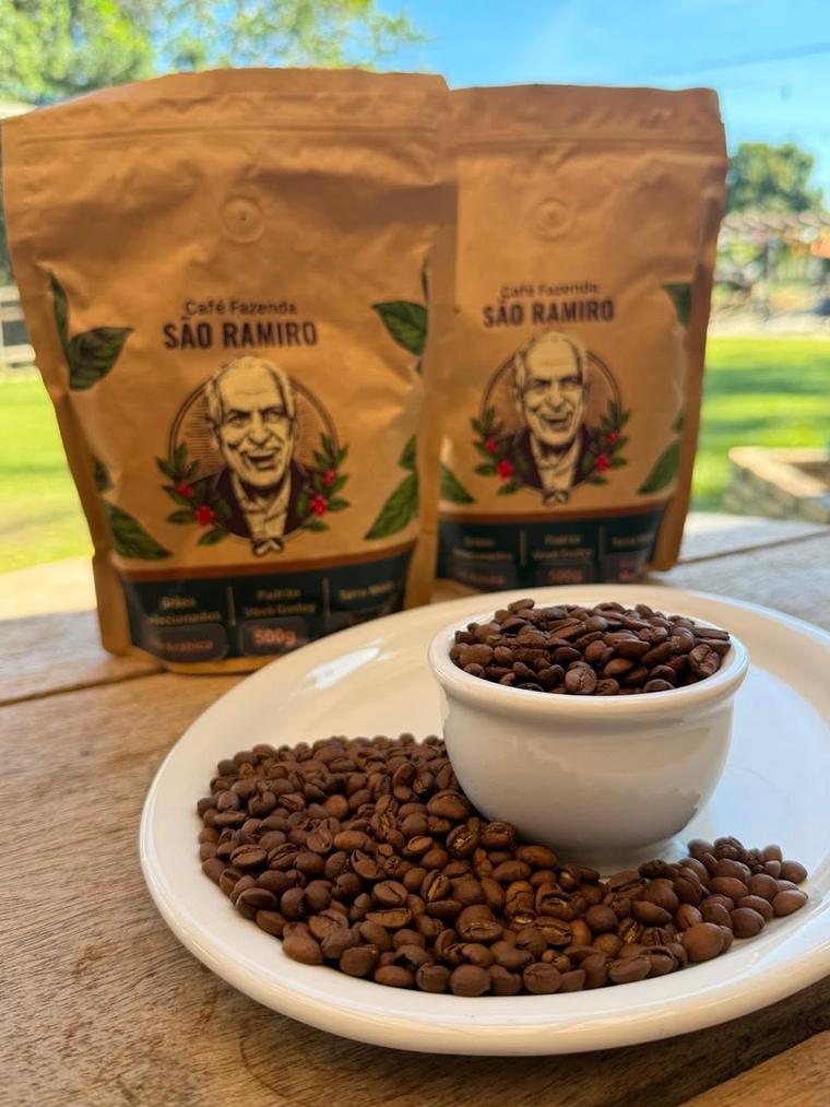 Pacotes do Café Fazenda São Ramiro ao lado de uma xícara com grãos de café torrado